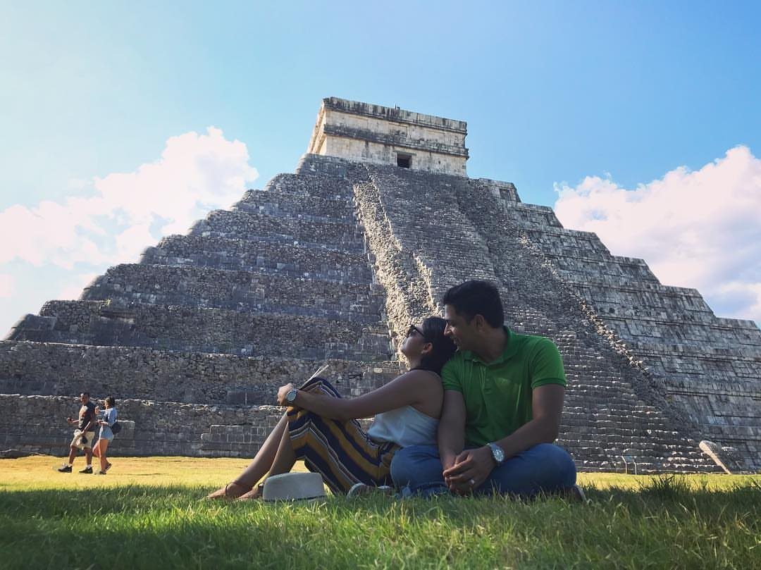 Couple sitting on grass in front of the Chichén Itzá Mayan pyramid