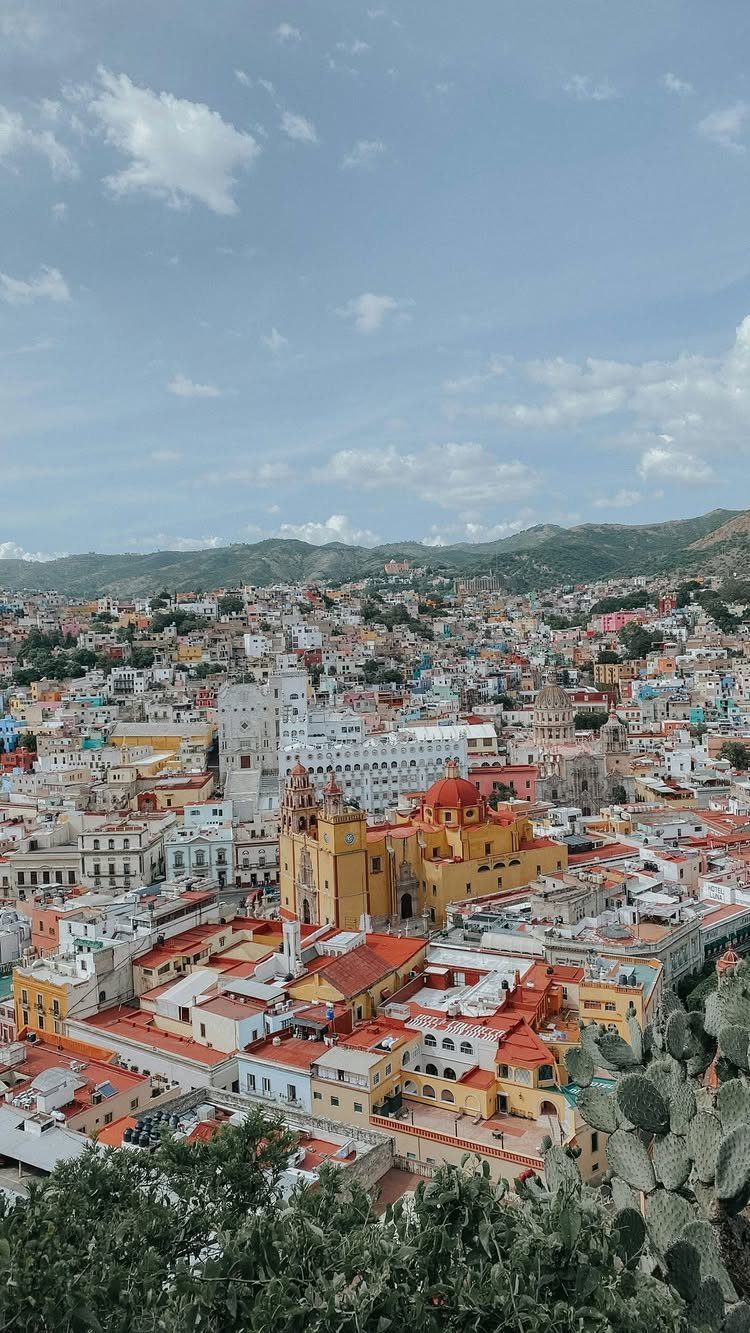 Colorful colonial city skyline with a yellow church and distant green mountains.