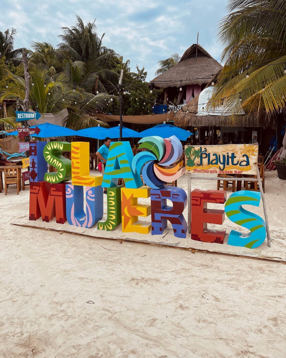 Colorful Isla Mujeres sign on a white sandy beach with palm trees.