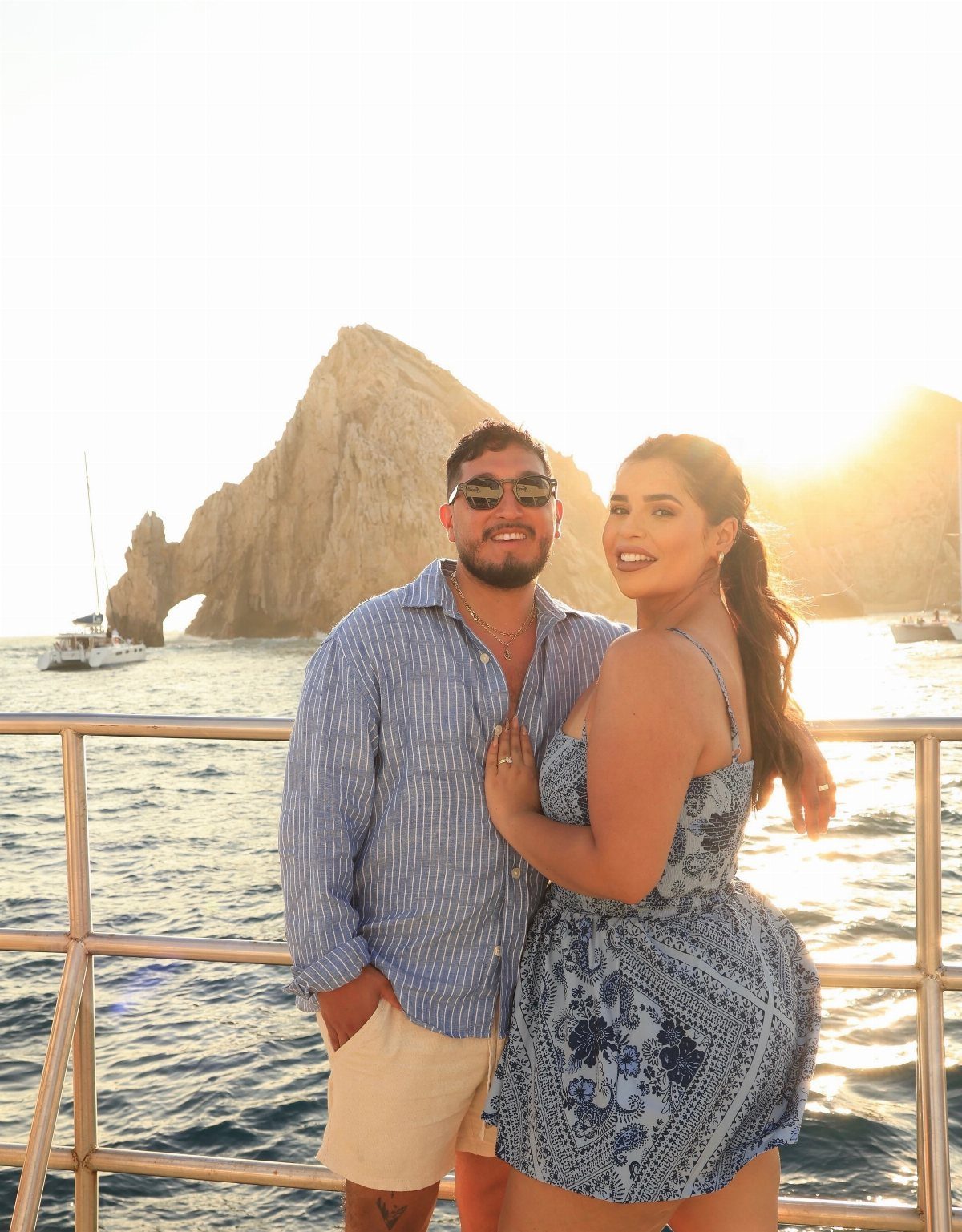 Couple posing on a boat with the El Arco rock formation in Los Cabos.