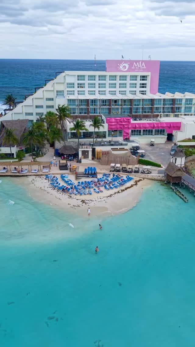 Mia Reef resort with white tiered architecture and blue beach chairs by turquoise water.