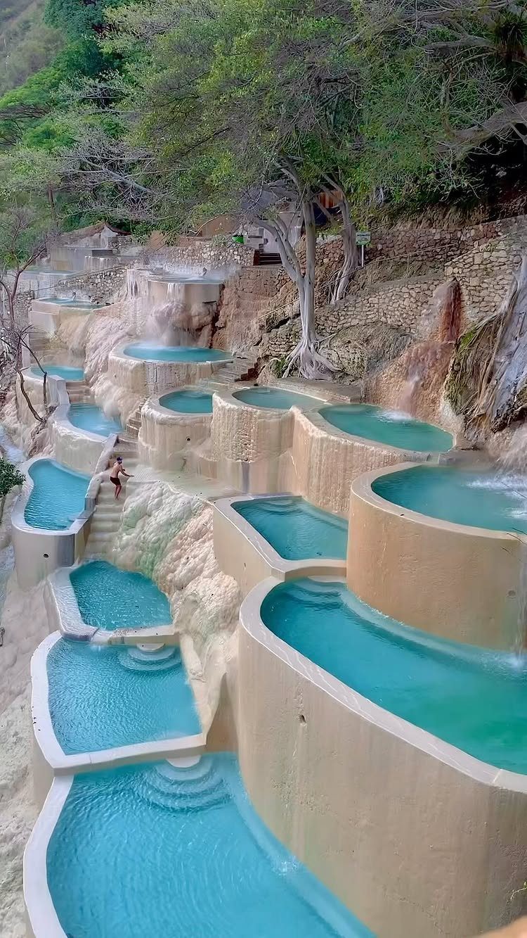 Tiered turquoise pools cascading down a rocky hillside surrounded by lush green trees.