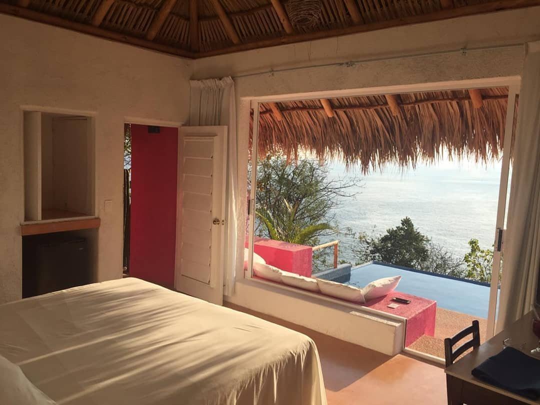 Bedroom with white bed and thatched ceiling overlooking a pool and ocean view