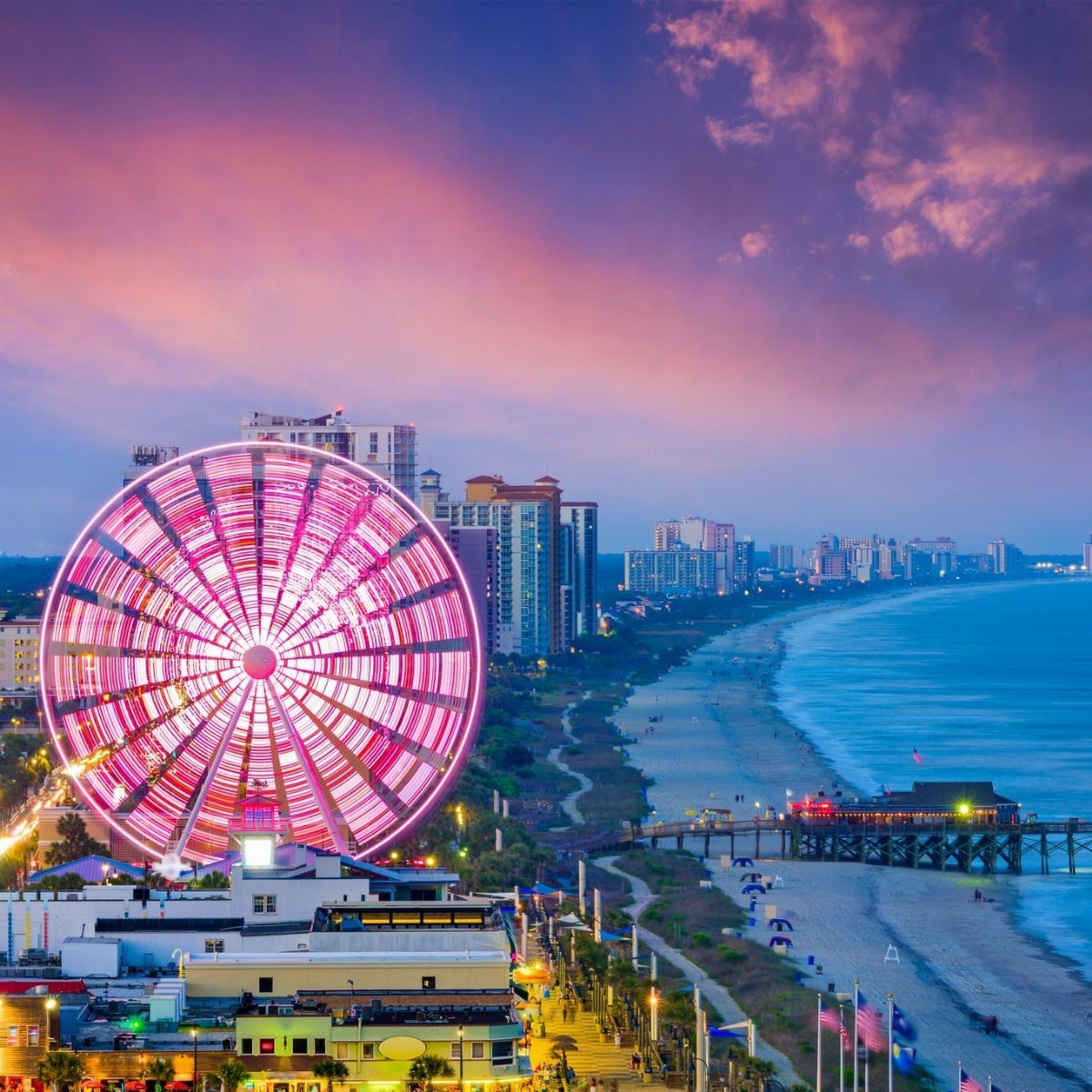 Illuminated SkyWheel Ferris wheel on the Myrtle Beach coastline during a colorful sunset.