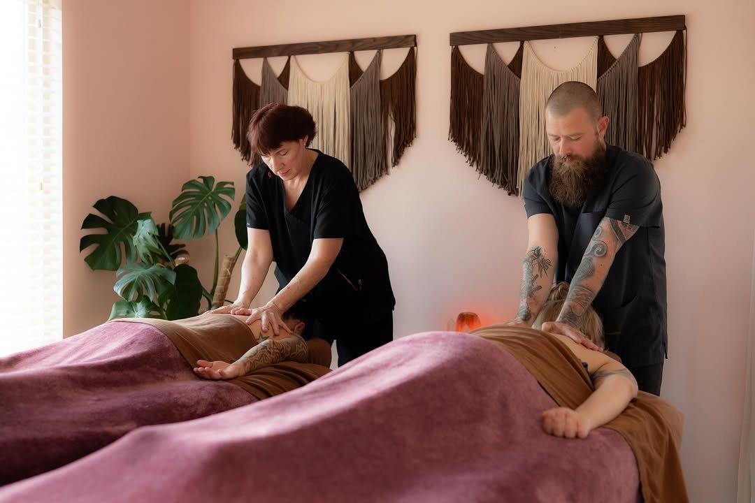 Two massage therapists giving simultaneous massages to a couple in a spa room.