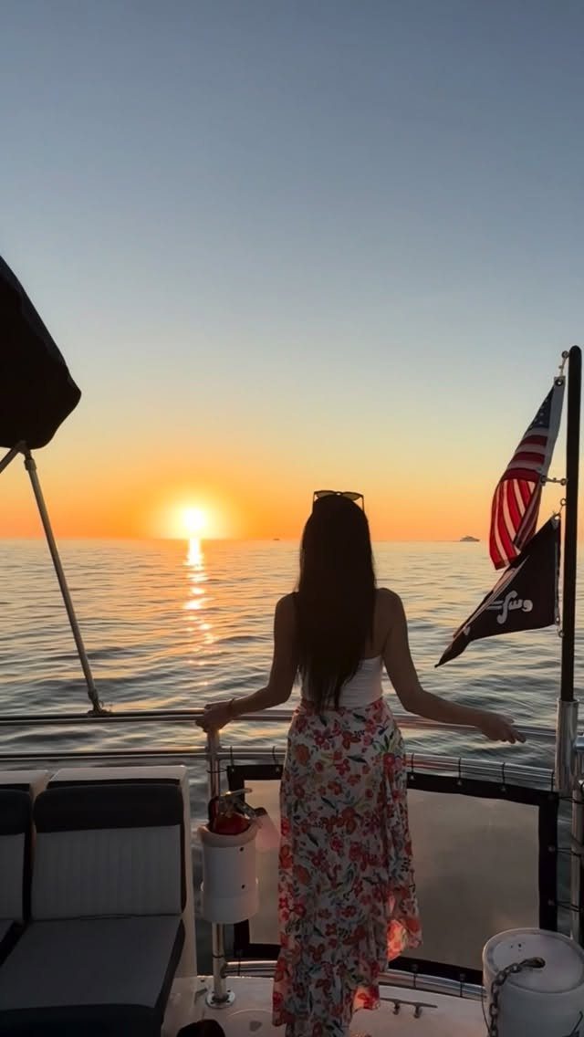 Woman in floral skirt watching a golden sunset from a boat deck.