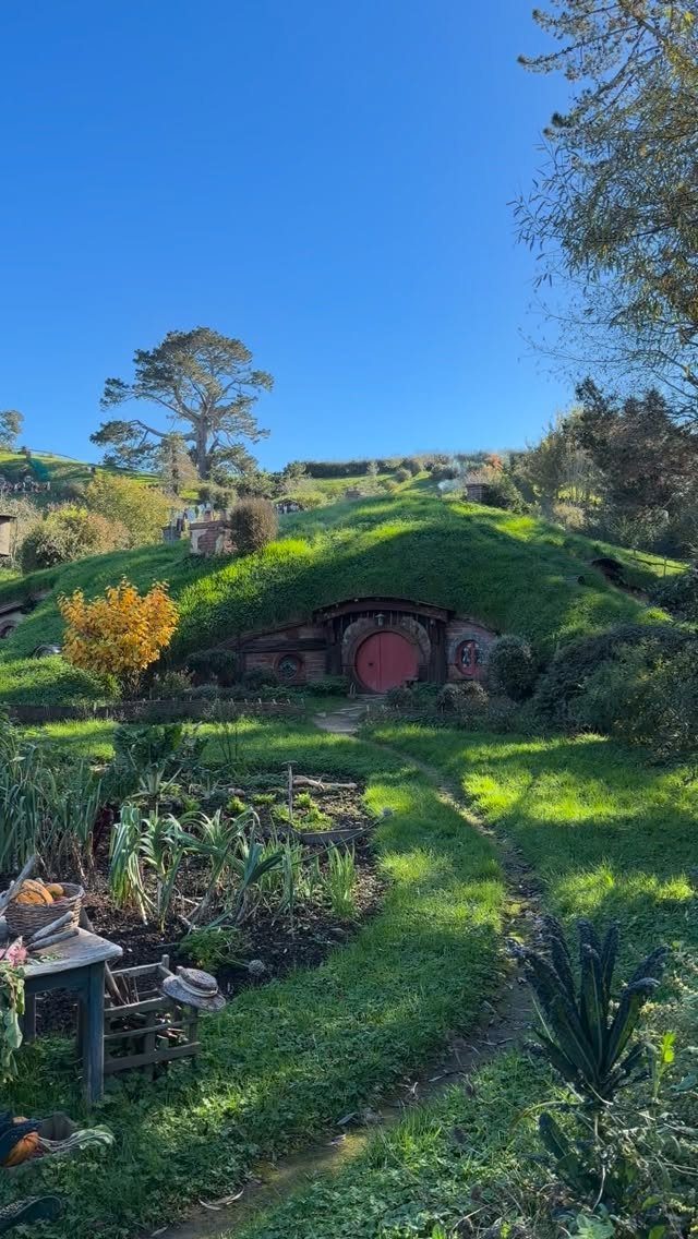 Round red hobbit hole door built into a lush green grassy hillside.