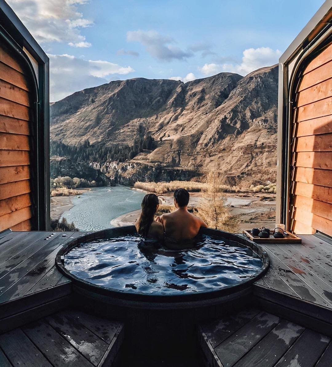 Couple soaking in an outdoor hot tub overlooking a scenic river and mountains.