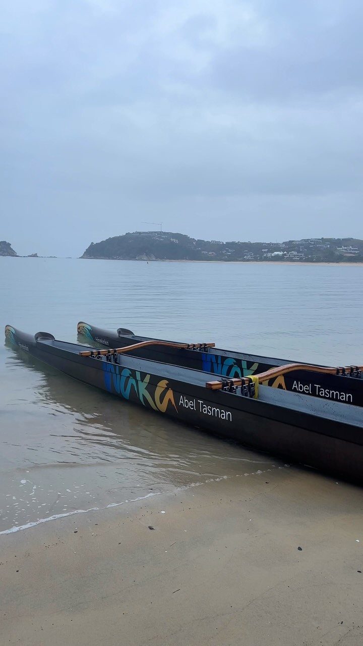 Two black tandem kayaks resting on a sandy beach in Abel Tasman