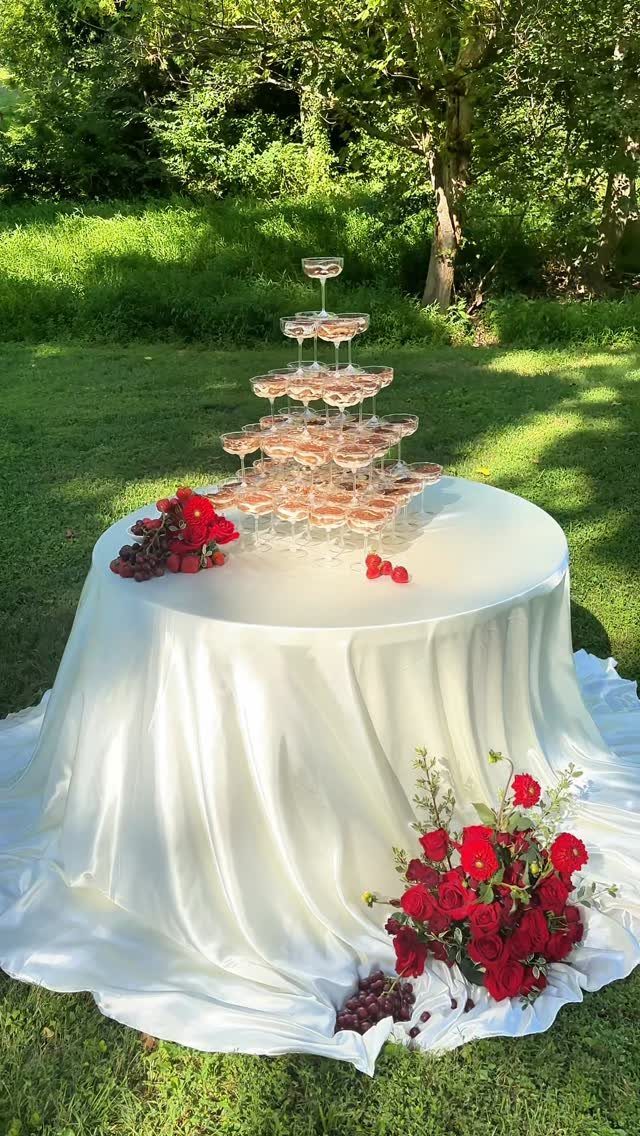 Champagne tower on a white satin table with red roses in a garden.