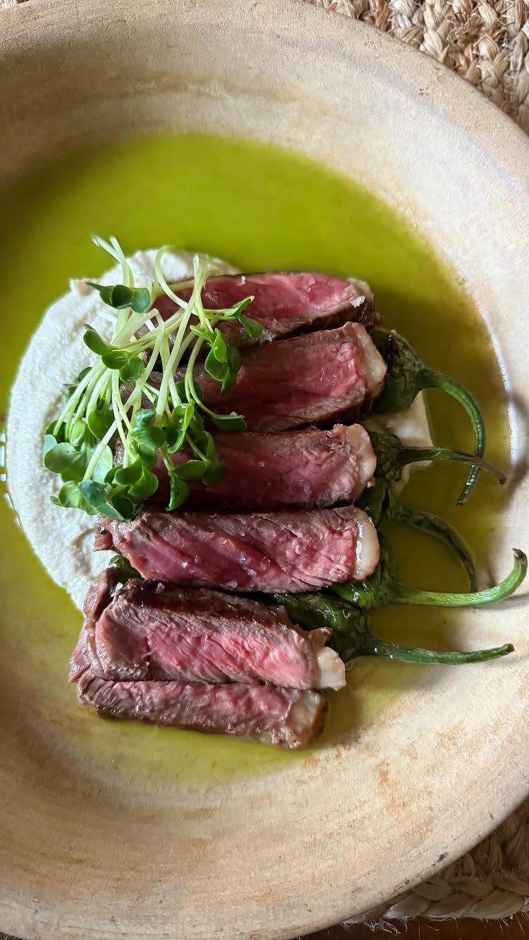 Medium-rare steak slices with microgreens and peppers in a ceramic bowl with oil.