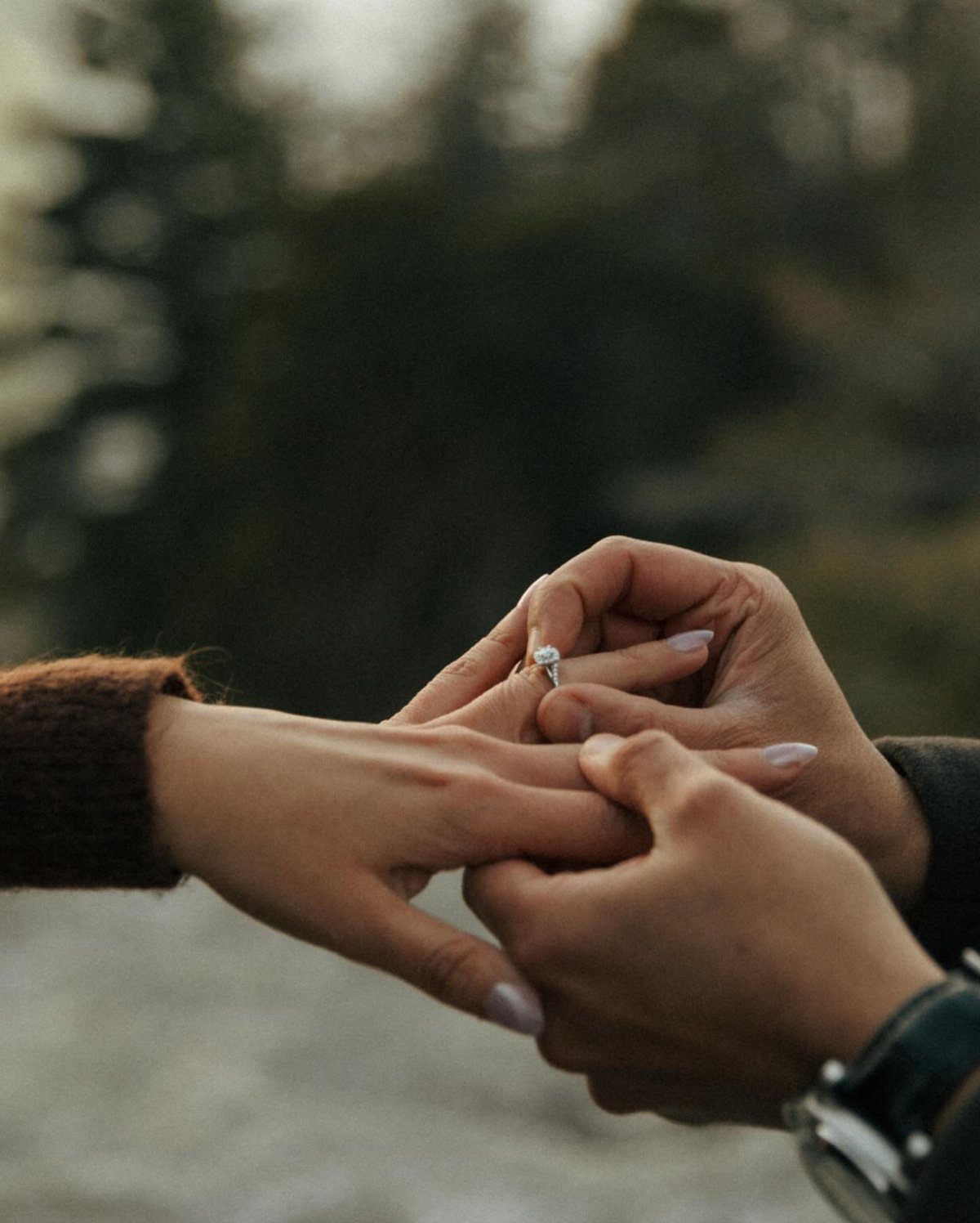 Hands of a couple as a diamond engagement ring is placed on a finger.