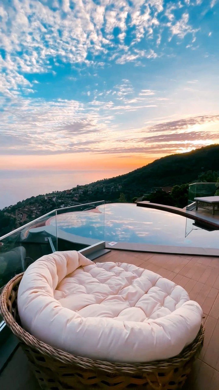 Luxury terrace with a wicker daybed and infinity pool overlooking a coastal hillside sunset.