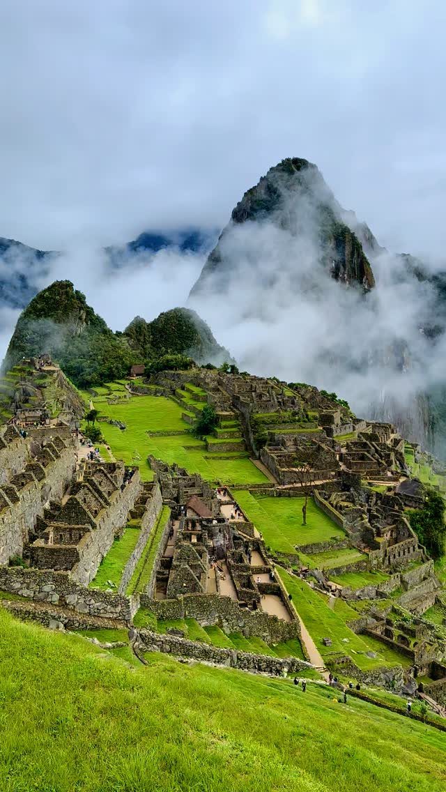 Machu Picchu ruins on a green mountain ridge surrounded by white clouds