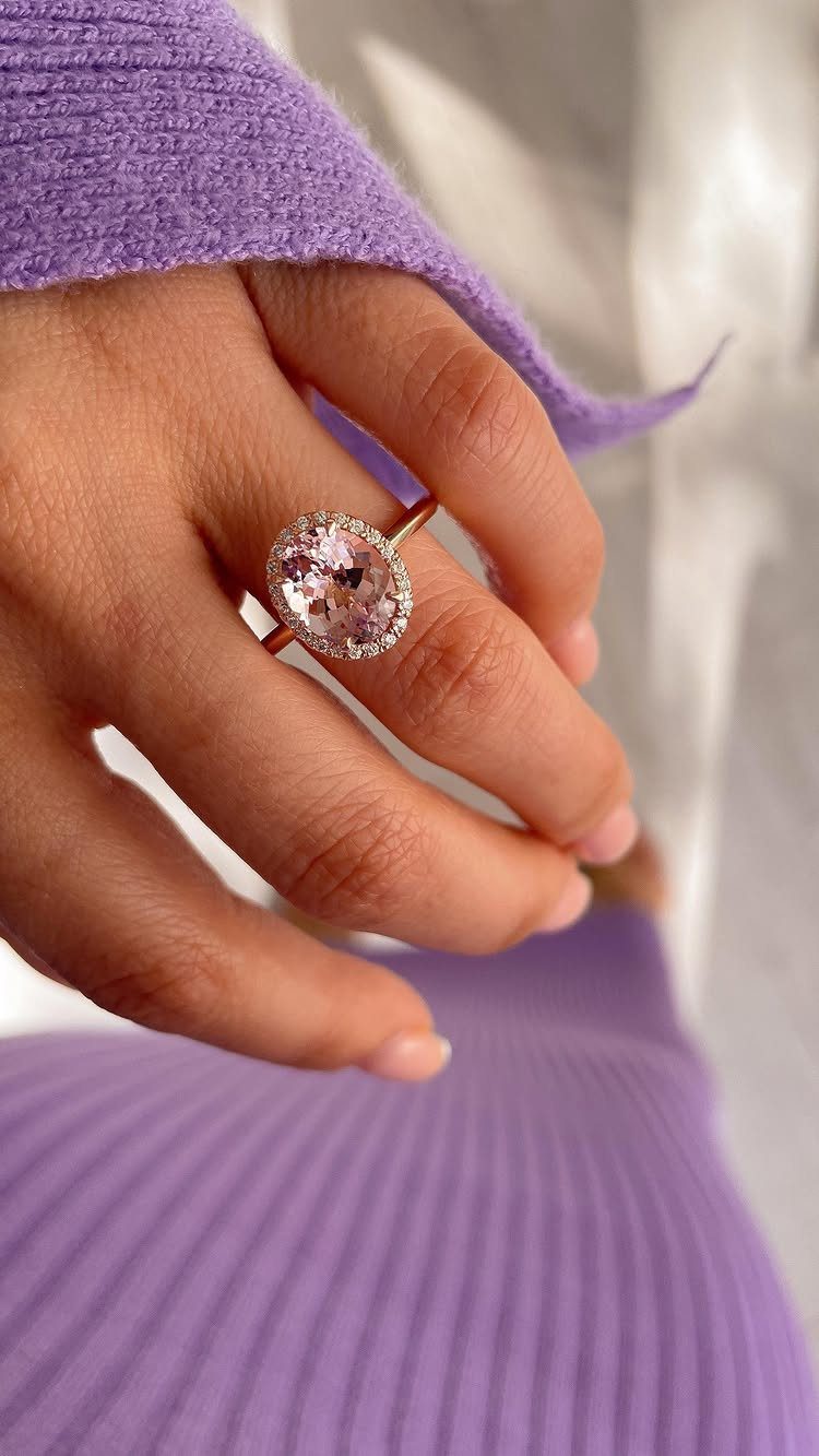 Rose gold ring with oval pink gemstone and diamond halo on a finger