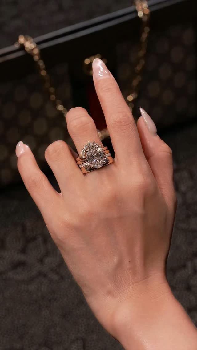 Stacked gold diamond engagement rings on a woman's finger against a dark handbag