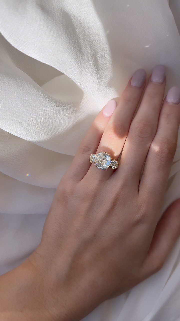 Three-stone diamond engagement ring on a woman's finger against white draped fabric