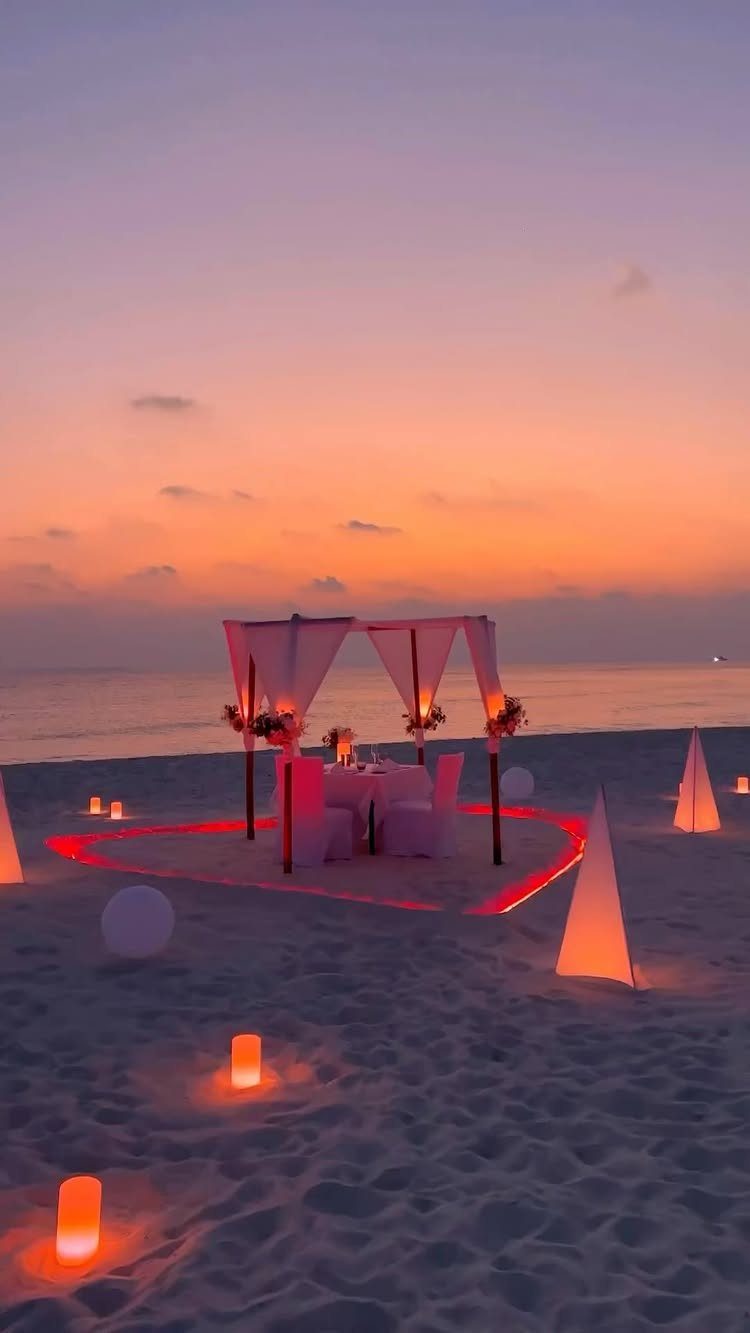 Romantic beach proposal setup with a canopy and heart-shaped glowing lights at sunset.