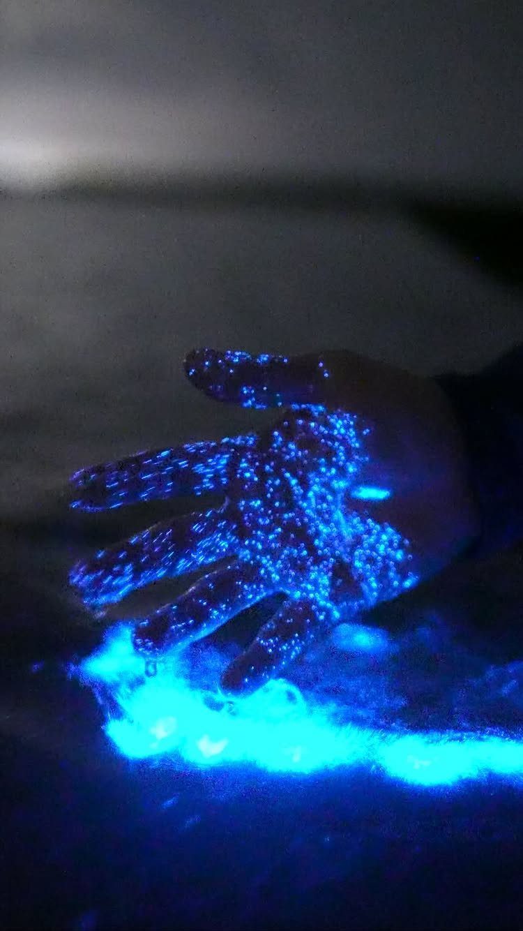 Hand touching glowing neon blue bioluminescent water in a dark night setting