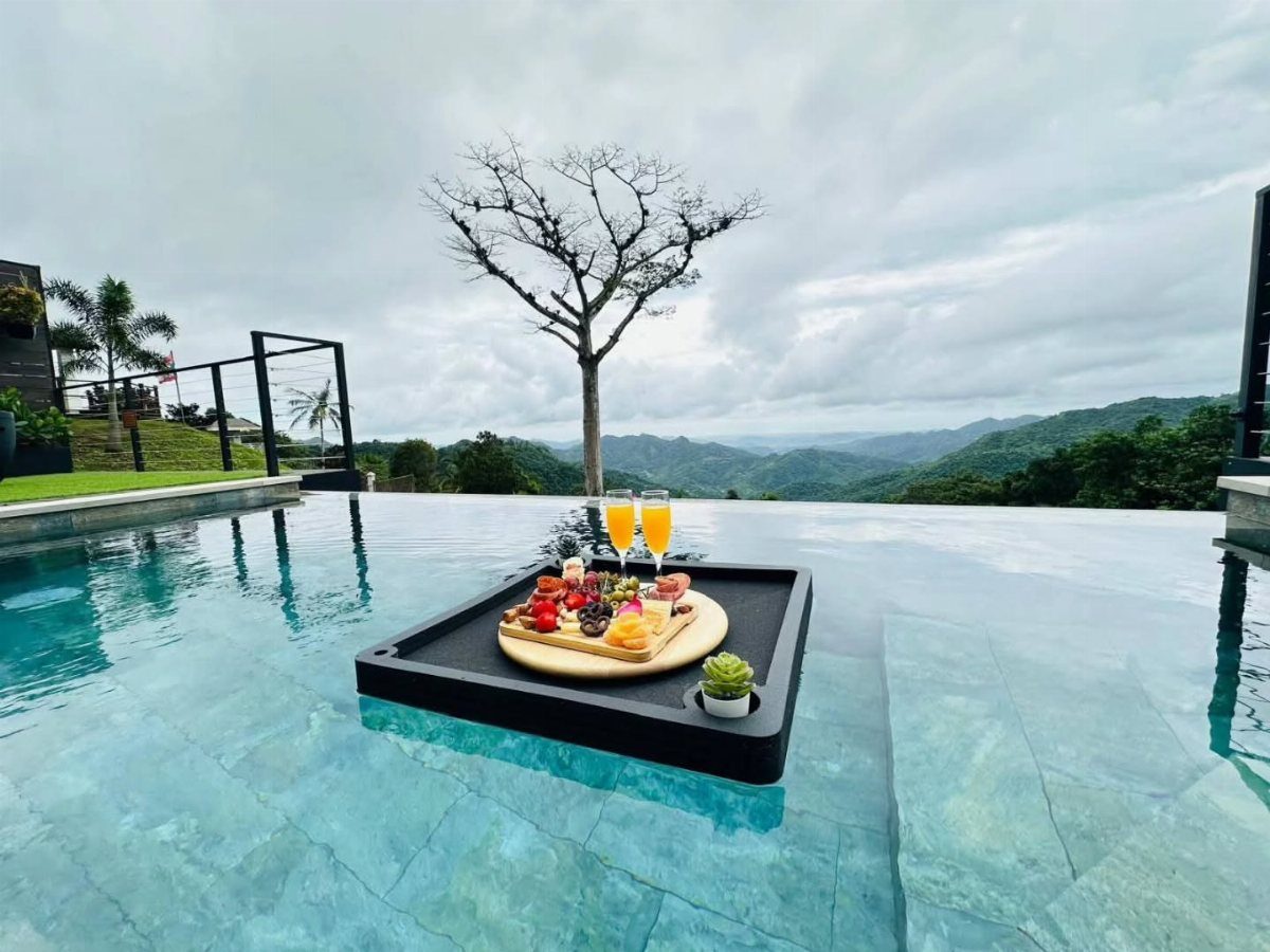 Floating breakfast tray with fruit and juice in an infinity pool overlooking mountains.
