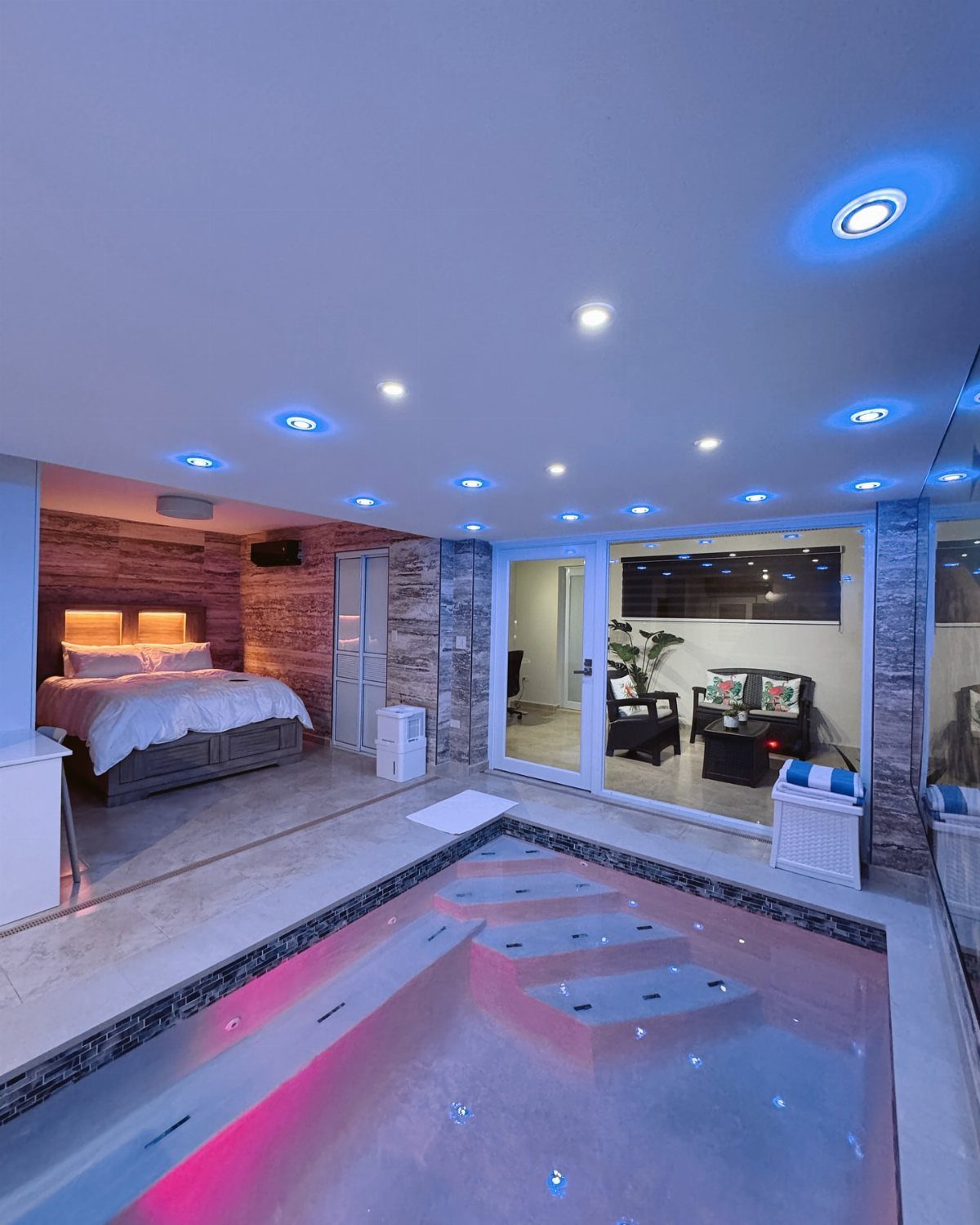 Luxury indoor suite with a bed and a glowing pink swimming pool.