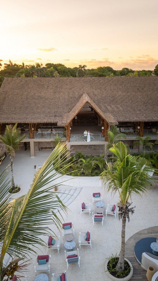 Tropical resort with thatched roof building, white sandy courtyard, and palm trees.