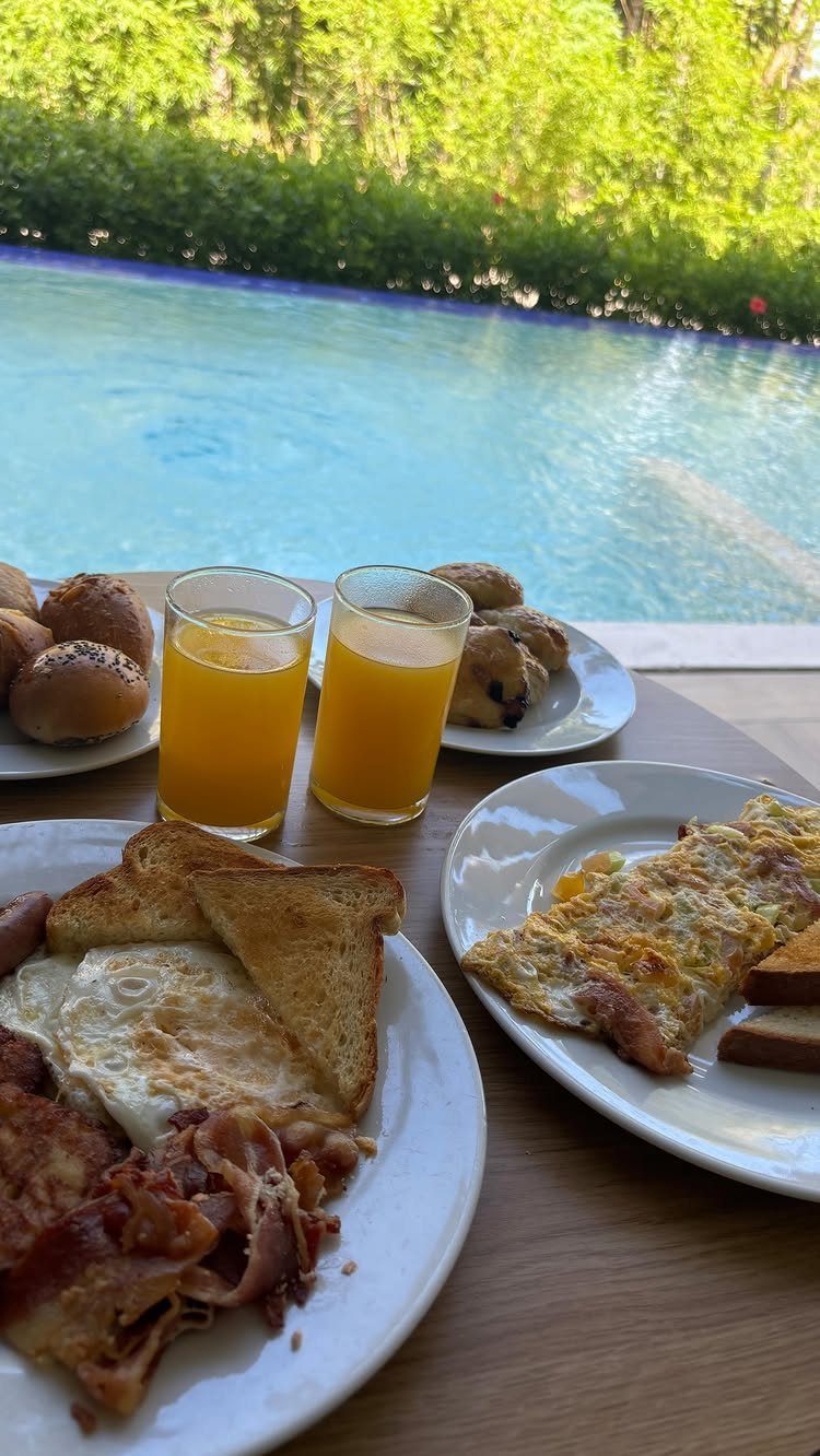 Breakfast spread with eggs, bacon, and orange juice by a blue swimming pool.