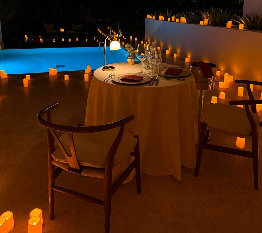 Romantic dinner table set for two with candles beside a blue swimming pool