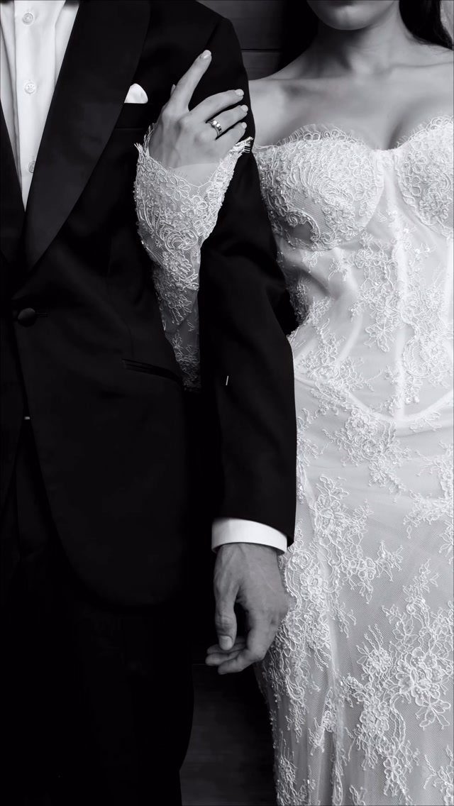 Bride in lace dress resting her ringed hand on groom's tuxedo shoulder