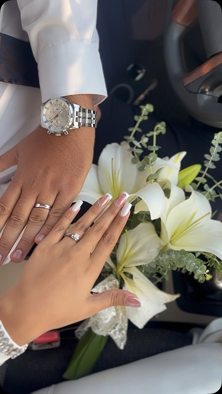 Hands with wedding rings resting on a bouquet of white lilies in a car.