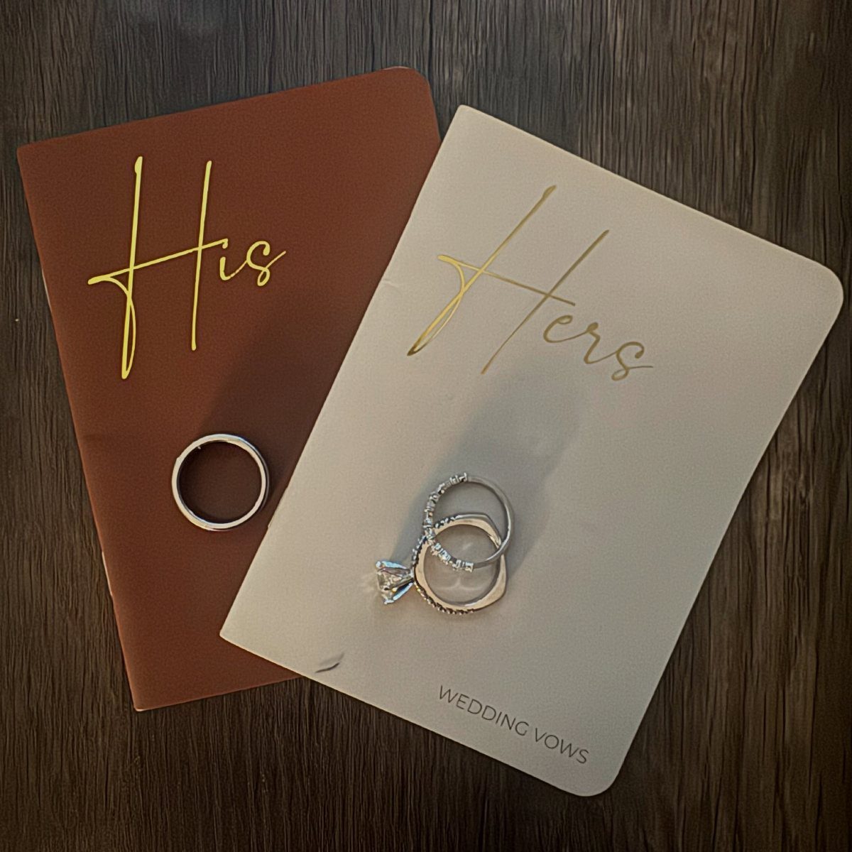 Wedding rings resting on brown and cream vow cards labeled His and Hers.