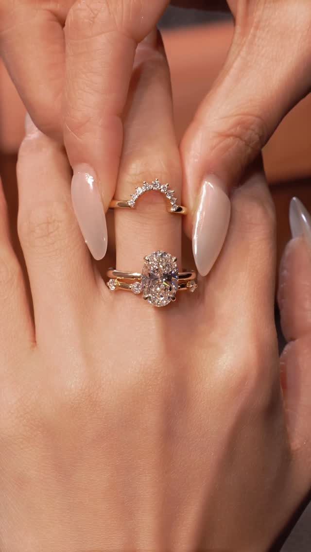 Gold engagement ring and curved diamond band stacked on a finger with pink nails