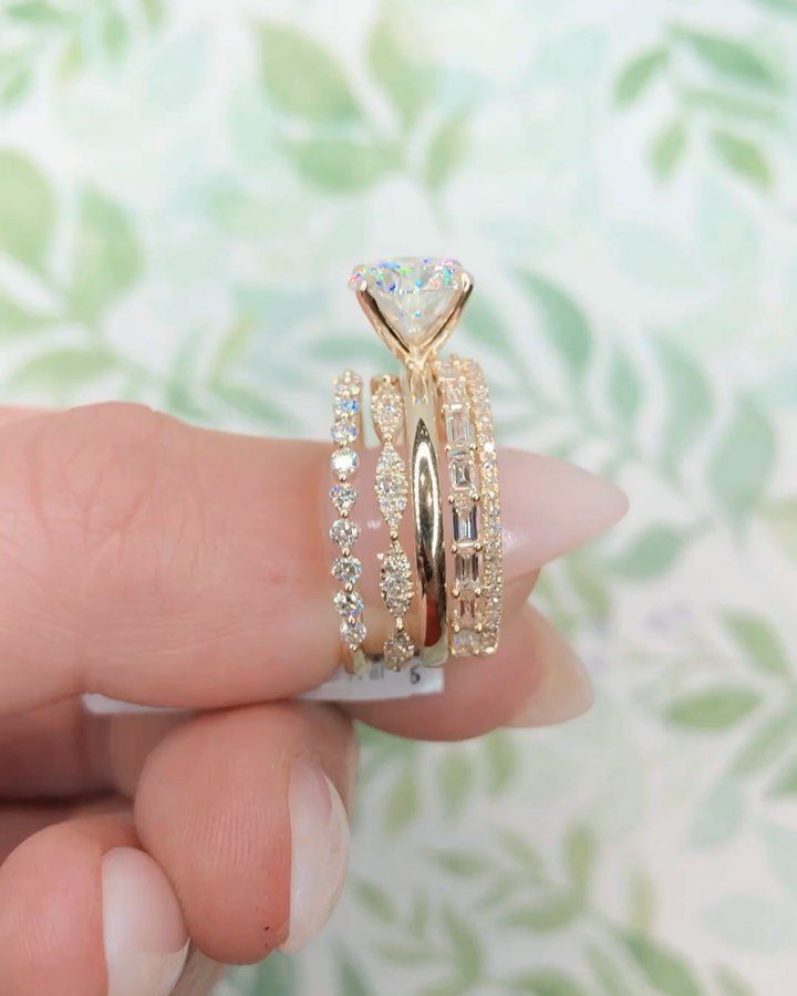 Three gold diamond rings stacked on a finger against a blurred green background.
