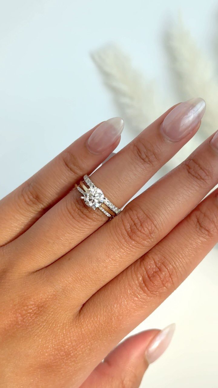 Three silver rings stacked on a finger, featuring a central diamond engagement ring.