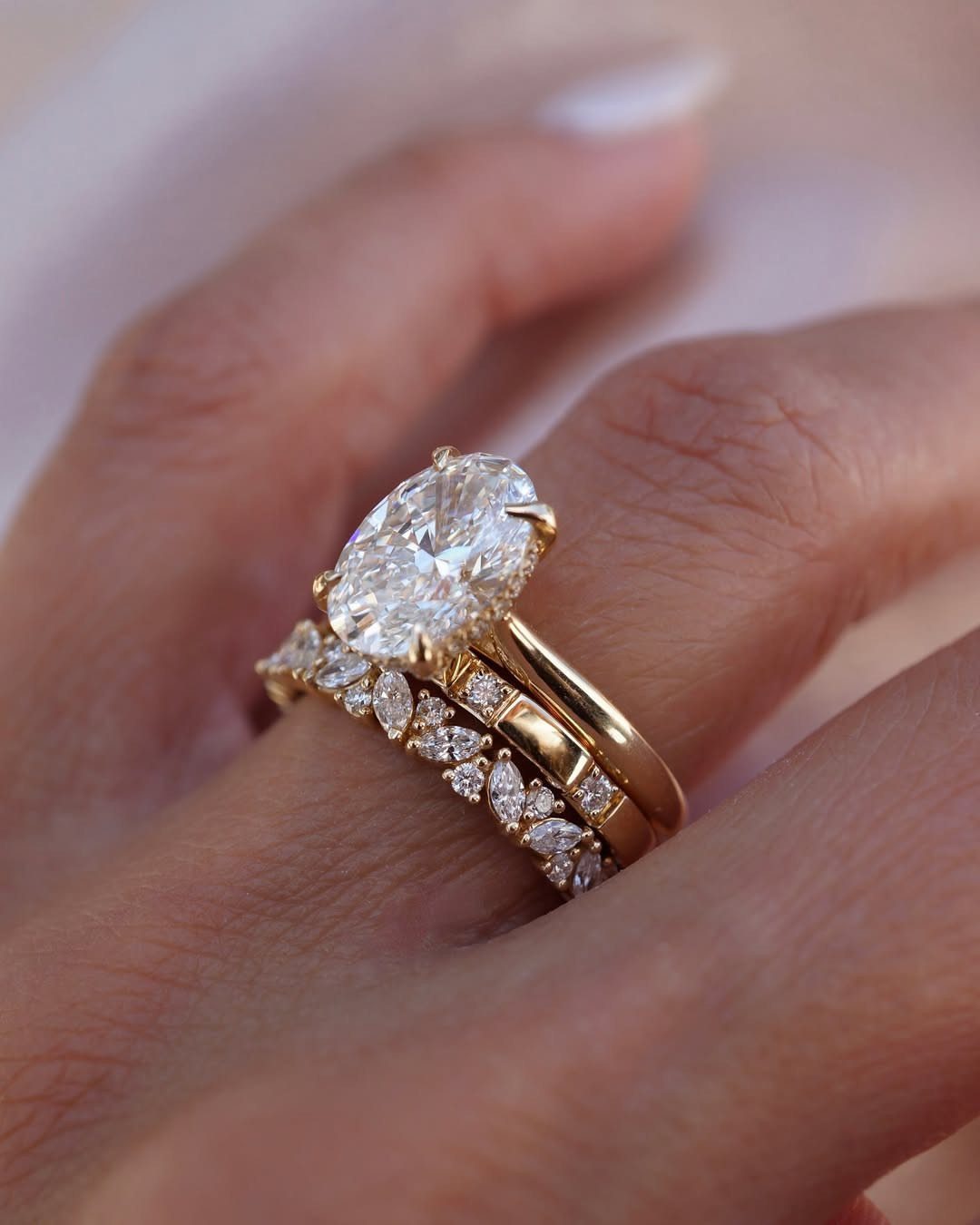 Three gold rings stacked on a finger, featuring a large oval diamond center stone.