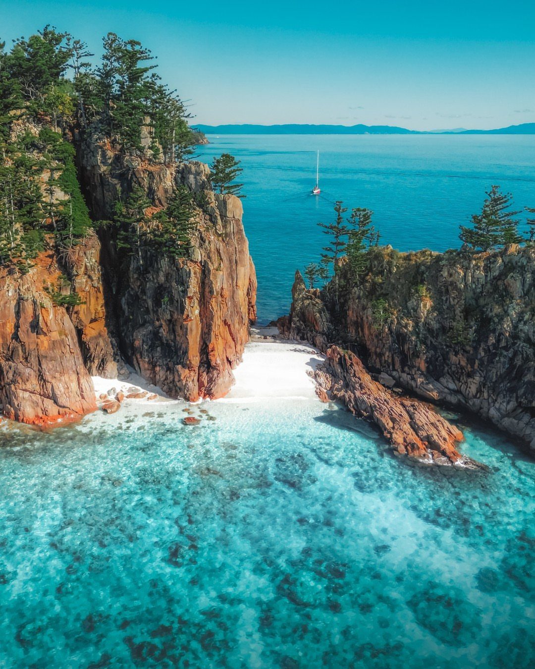 Secluded white sand beach nestled between rocky cliffs and turquoise ocean water.