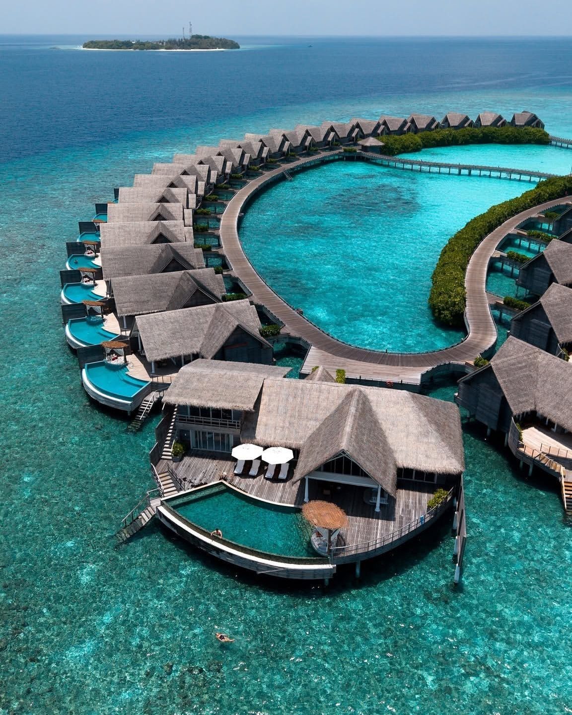 Overwater bungalows with thatched roofs and private pools in a turquoise ocean lagoon.