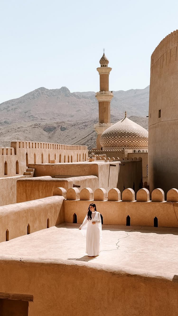 Woman in white dress standing on the rooftop of an ancient Omani fort.
