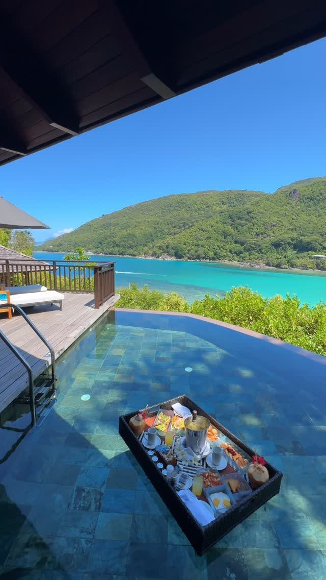 Floating breakfast tray in an infinity pool overlooking a tropical bay and mountains.