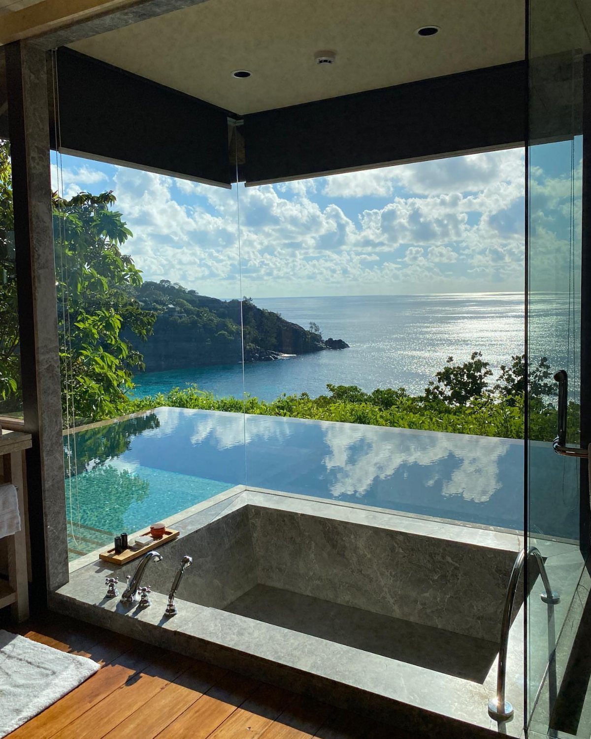 Luxury stone bathtub and infinity pool overlooking a tropical ocean coastline.