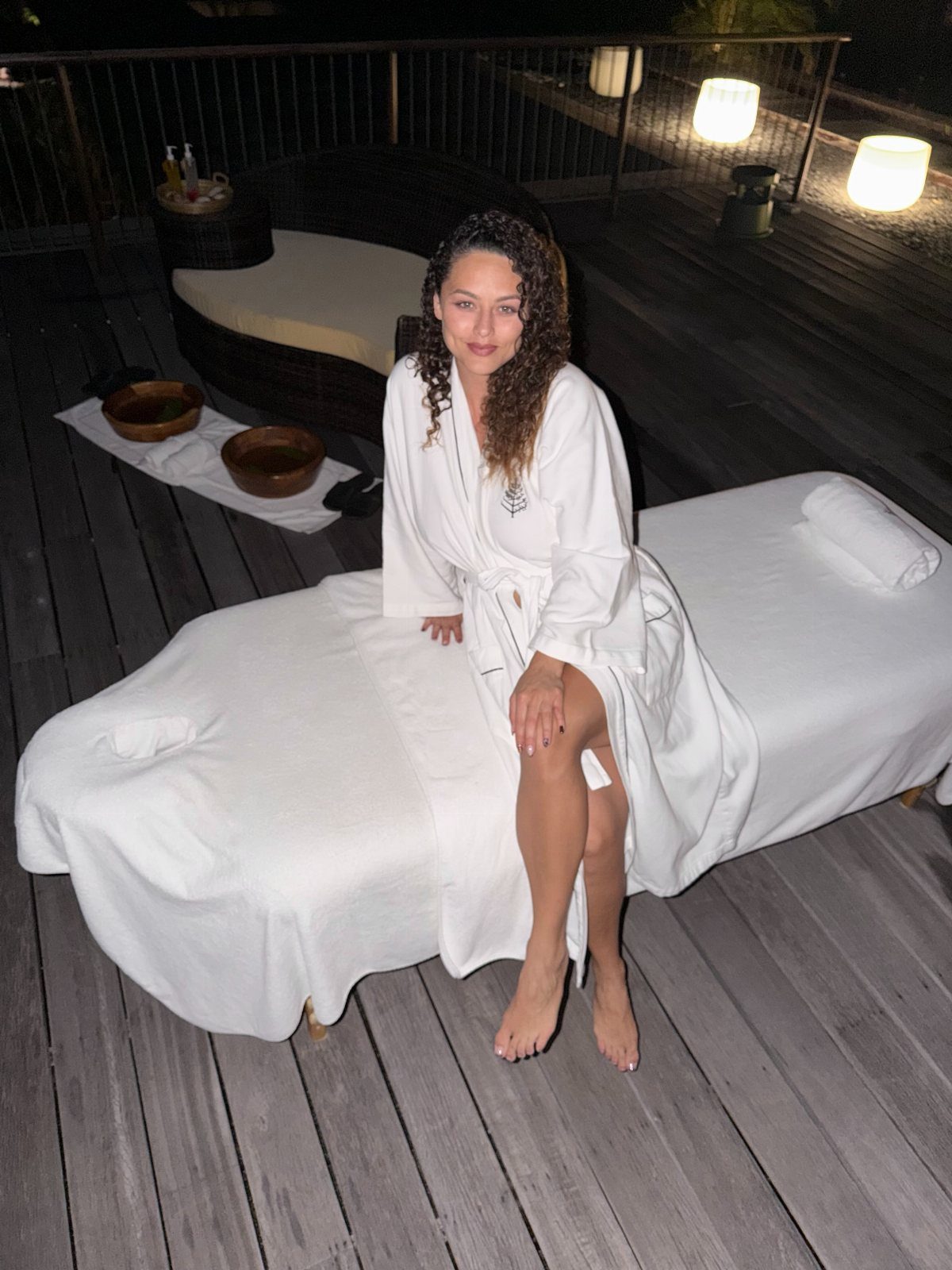 Woman in white bathrobe sitting on a massage table on a wooden deck
