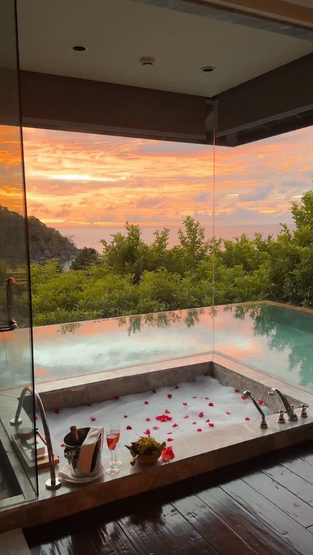 Luxury bathtub with rose petals and champagne overlooking a tropical sunset ocean view