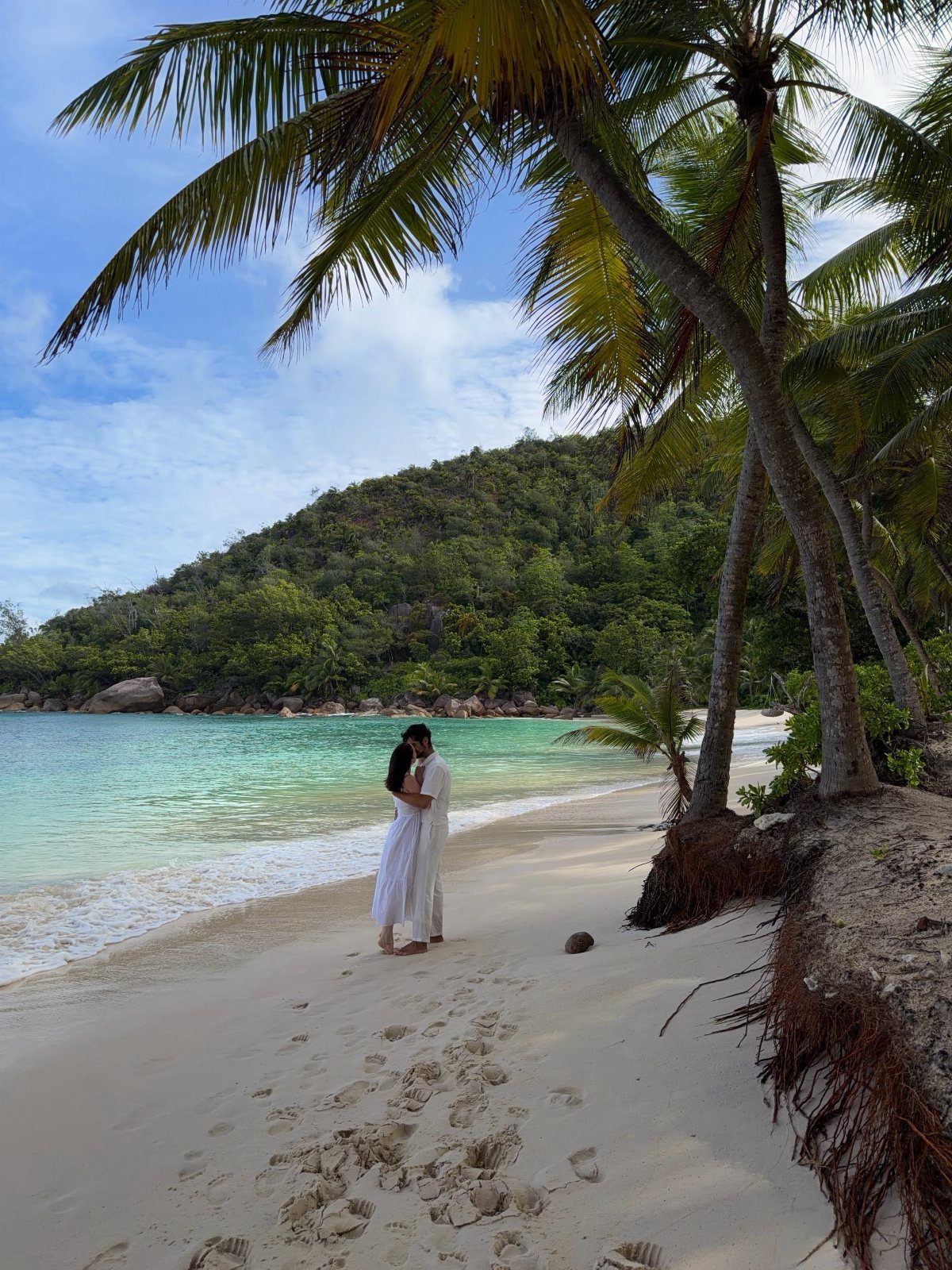 Couple embracing on a white sand beach with turquoise water and palm trees.