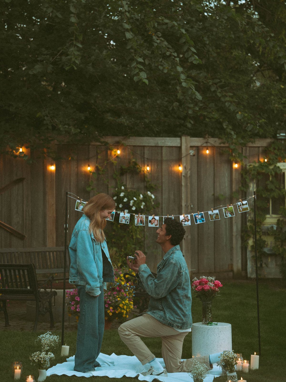Man proposing to a woman in a decorated backyard with string lights and photos.