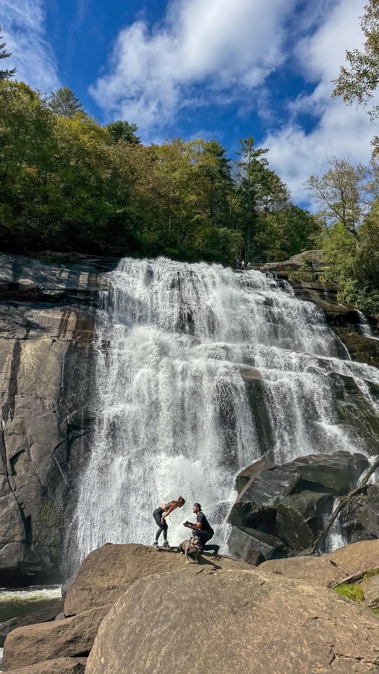 Man proposing to a woman on rocks in front of a large waterfall