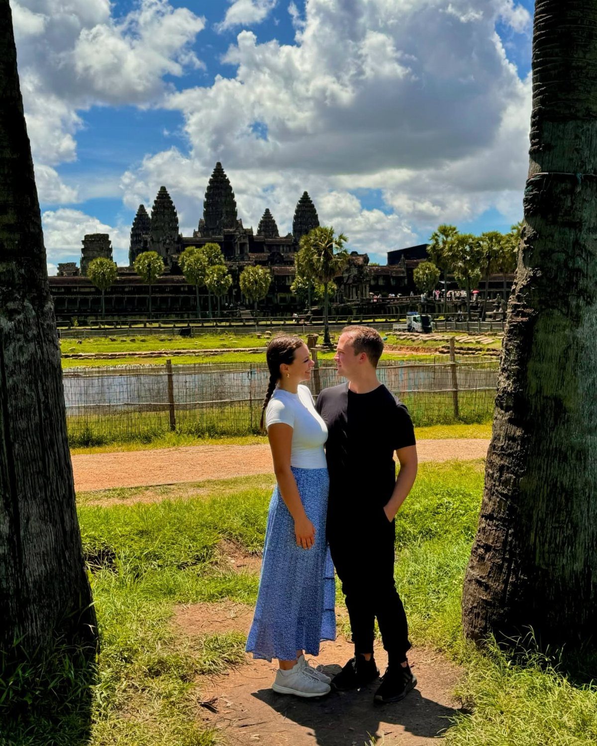 Couple standing in front of the Angkor Wat temple complex under a cloudy sky
