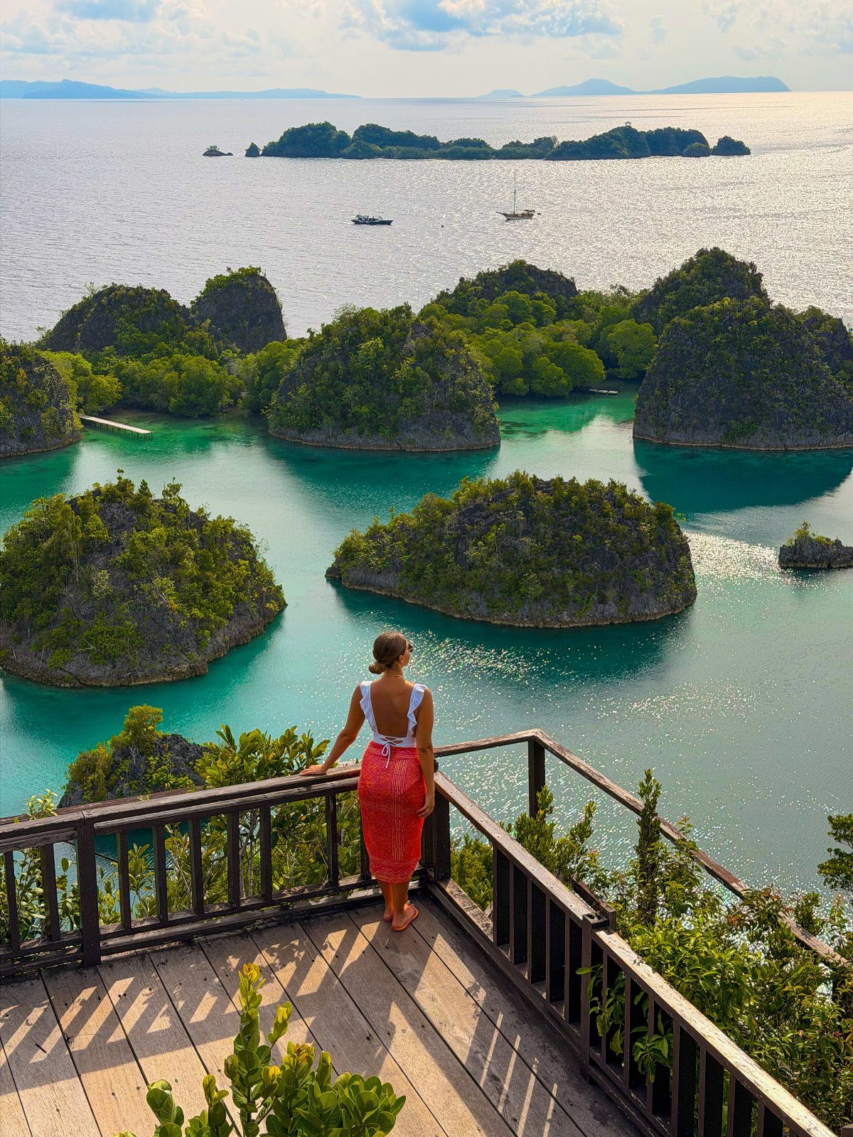 Woman overlooking turquoise waters and lush green limestone islands from a wooden platform.