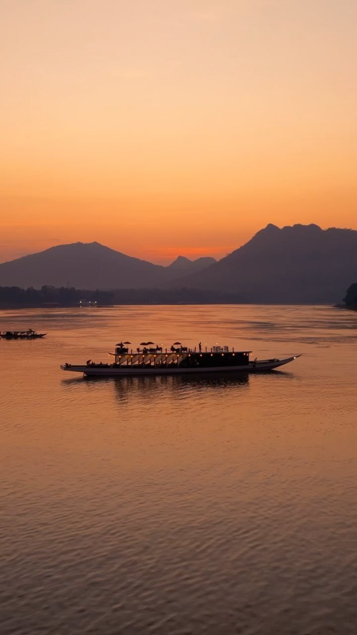 Long boat with passengers on a river at sunset with silhouetted mountains