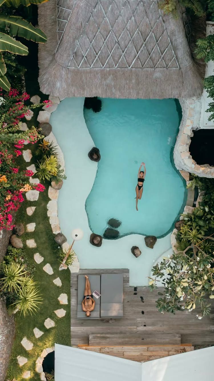 Tropical resort pool with a swimmer and a person lounging on a sunbed.