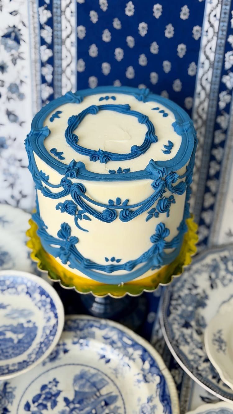 White cake with blue chinoiserie piping on a yellow stand among porcelain plates.
